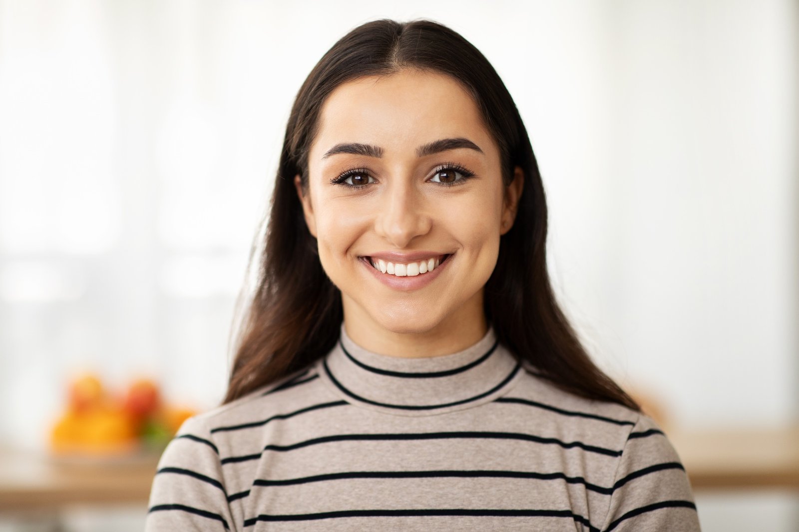 Headshot of cheerful young pretty arab lady looking at camera in light living room interior